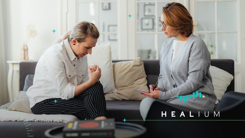 A woman sits with her therapist during a session. The Healium logo is in the bottom right.