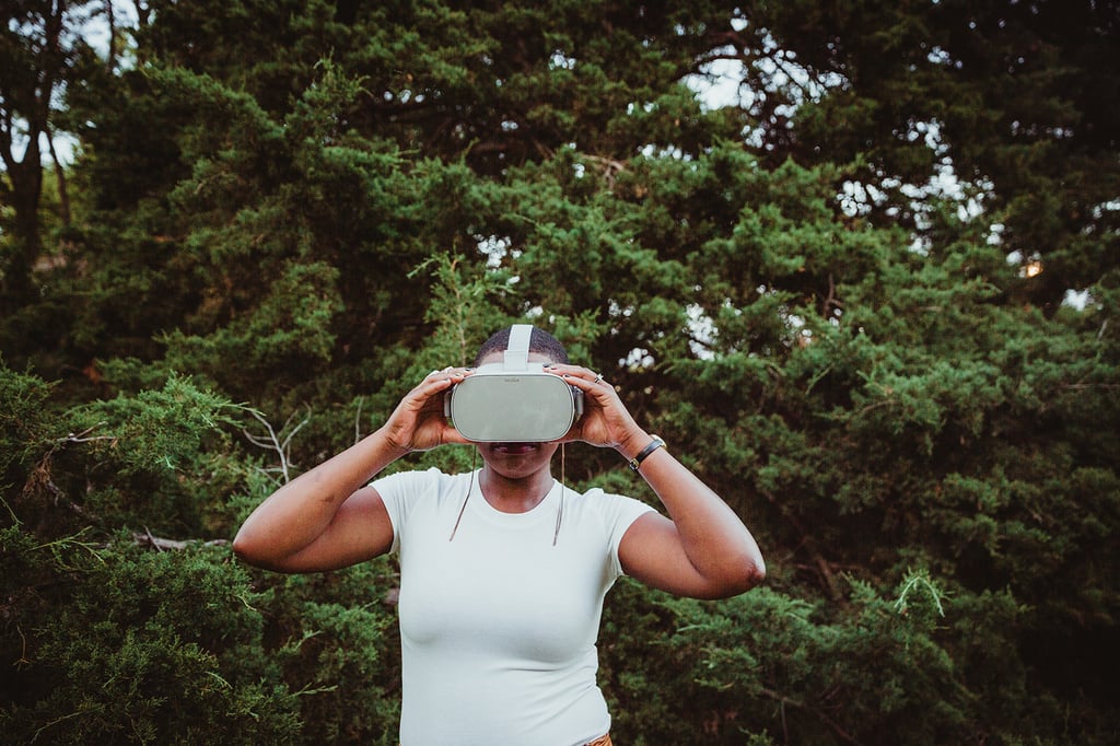 Chrystal wears her virtual reality headset while standing in front of green bushes and trees