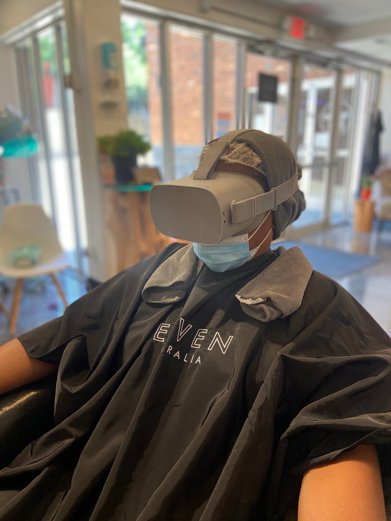 A woman sits in the salon chair getting a deep conditioning treatment while wearing a virtual reality headset