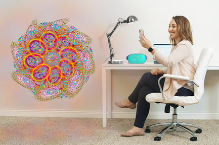 Wendy sits at her desk with computer, lamp, and Oculus Go headset. She uses her phone to view a colorful flower figure