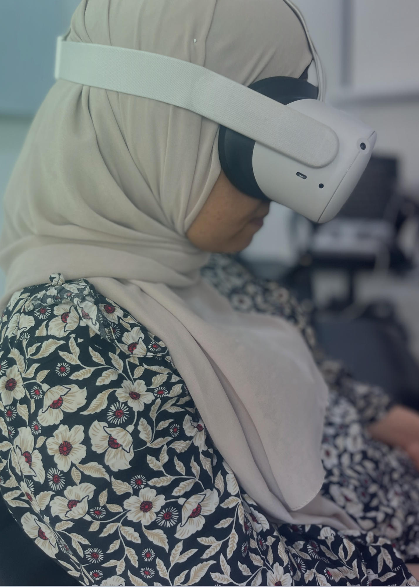 Women wears VR goggles while in a Healium experience. She wears a light colored hijab and floral patterned shirt.