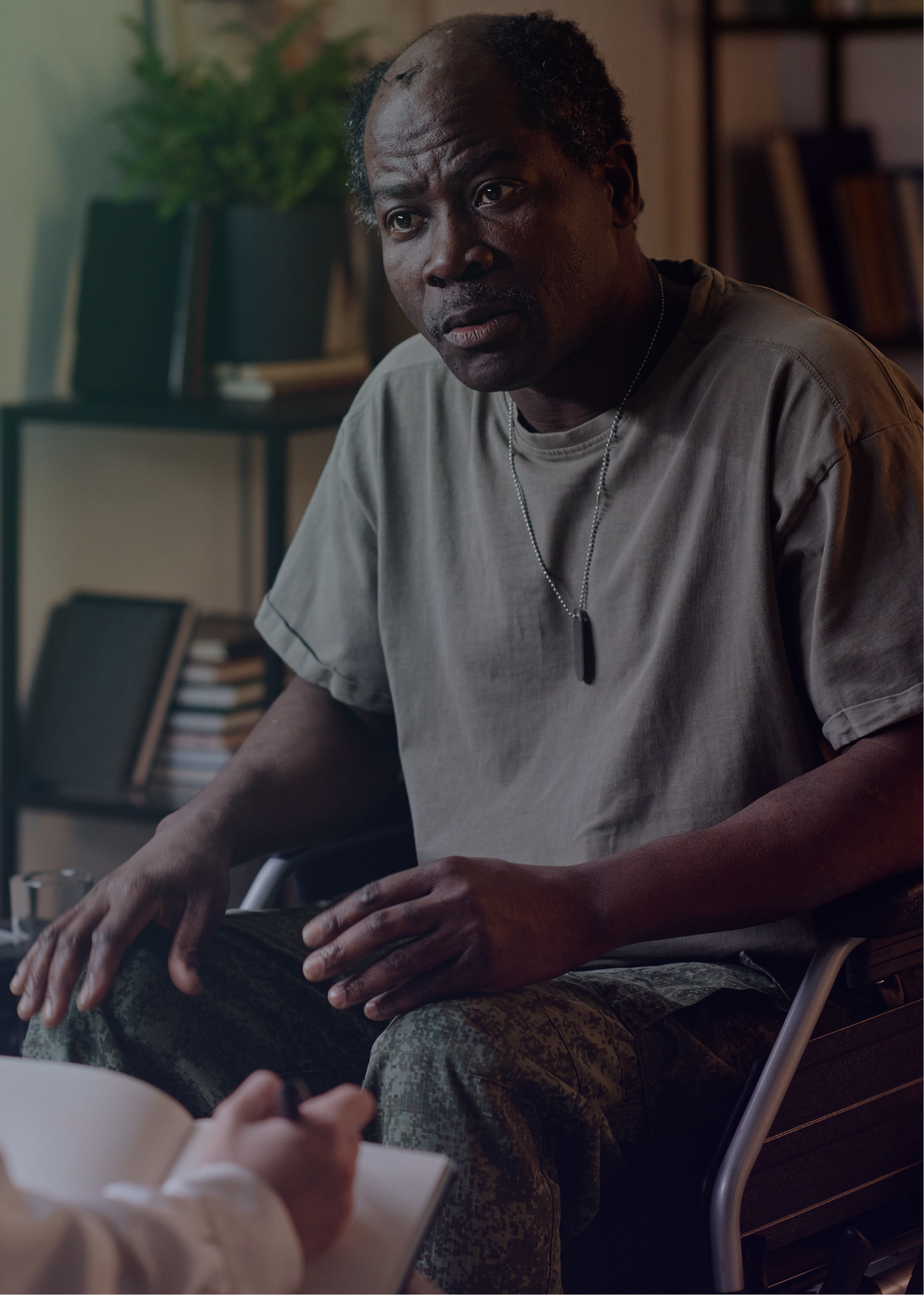 Man sits looking stressed in a wheelchair with a military ID tag on. 