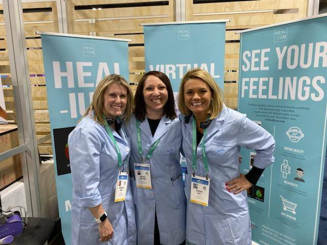 Wendy stands in the middle of Sarah and Michele at the CES conference. There are three pull up banner stands behind them.